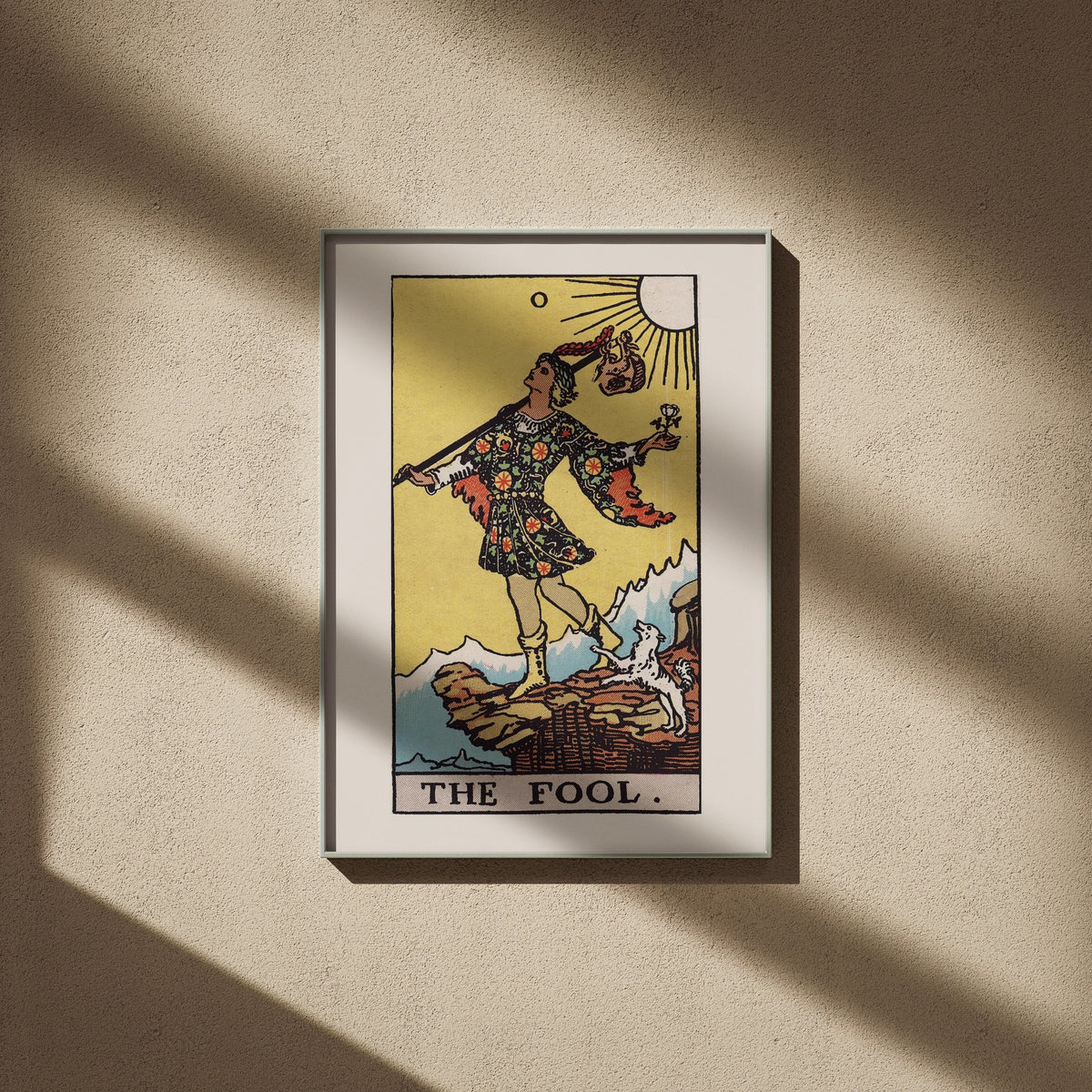 Le Mat - Arcane 0 du Tarot Rider-Waite, affiche encadrée sur un mur beige, ombres de fenêtre