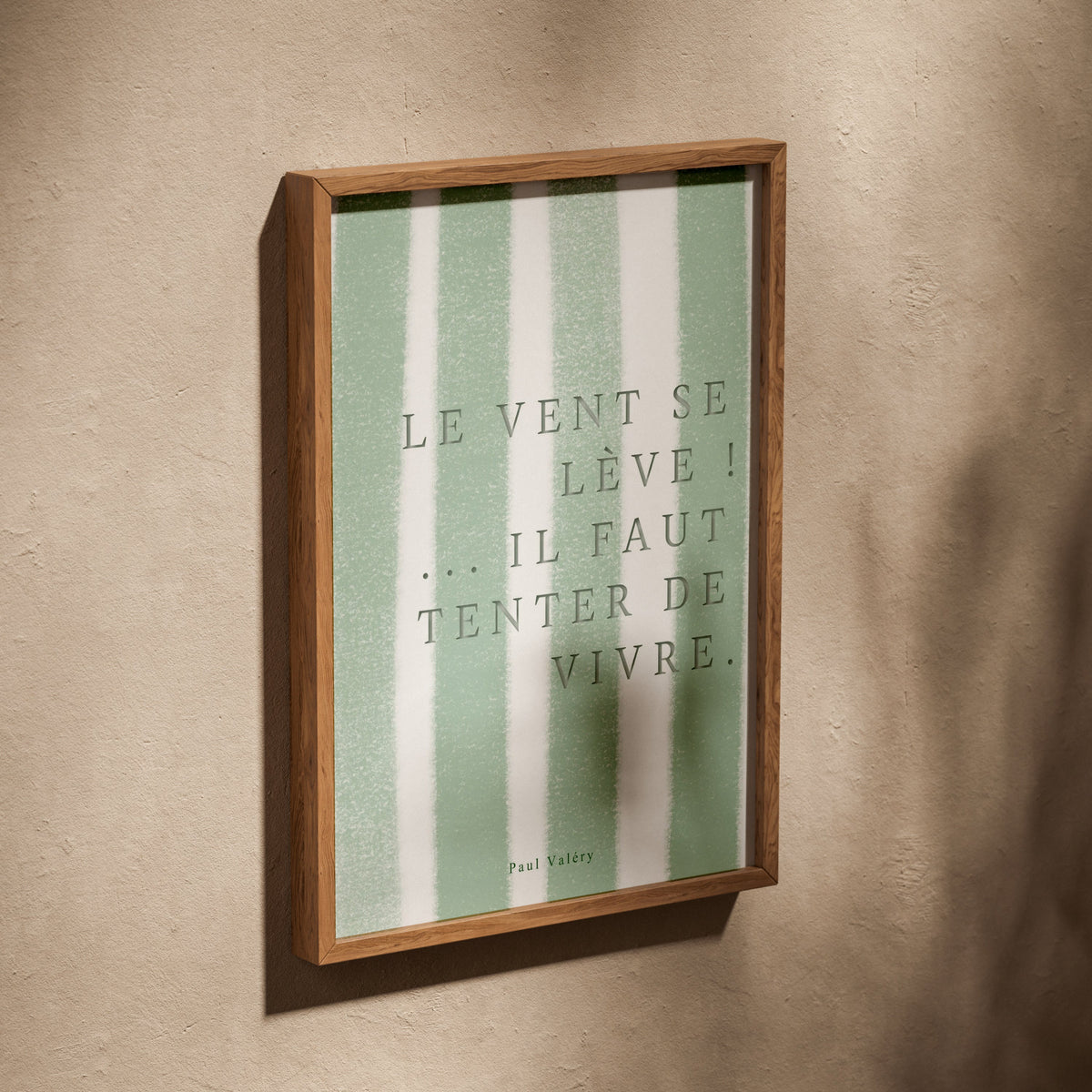 Affiche citation "Le vent se lève… il faut tenter de vivre", affiche dans un cadre en chêne posé de biais sur un mur texturé