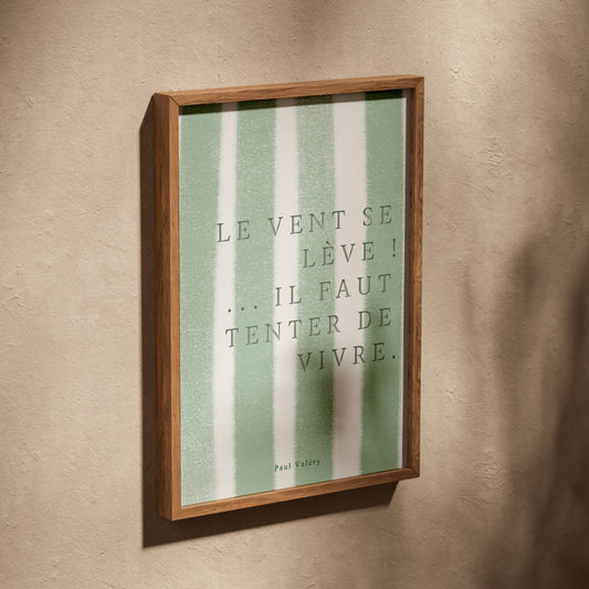 Affiche citation "Le vent se lève… il faut tenter de vivre", affiche dans un cadre en chêne posé de biais sur un mur texturé