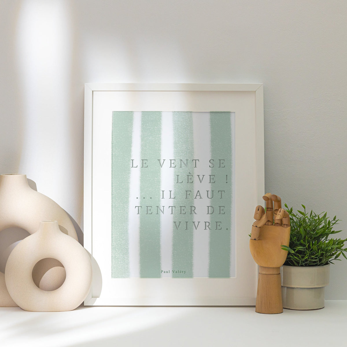 Affiche citation "Le vent se lève… il faut tenter de vivre", affiche encadrée posée près d'un vase blanc, lumière rasante
