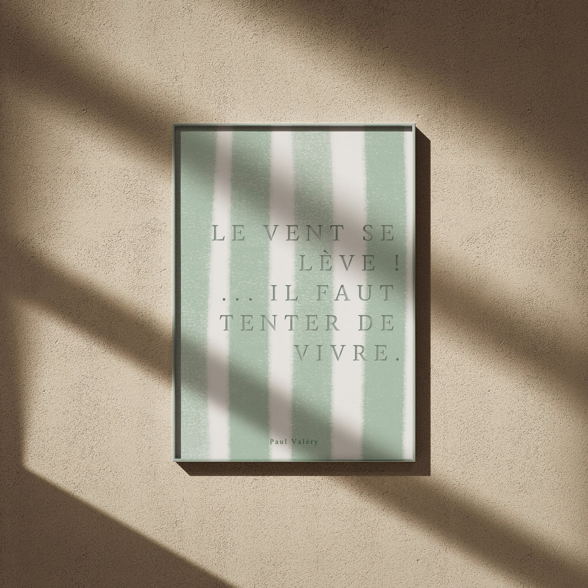 Affiche citation "Le vent se lève… il faut tenter de vivre", affiche encadrée sur un mur beige, ombres de fenêtre