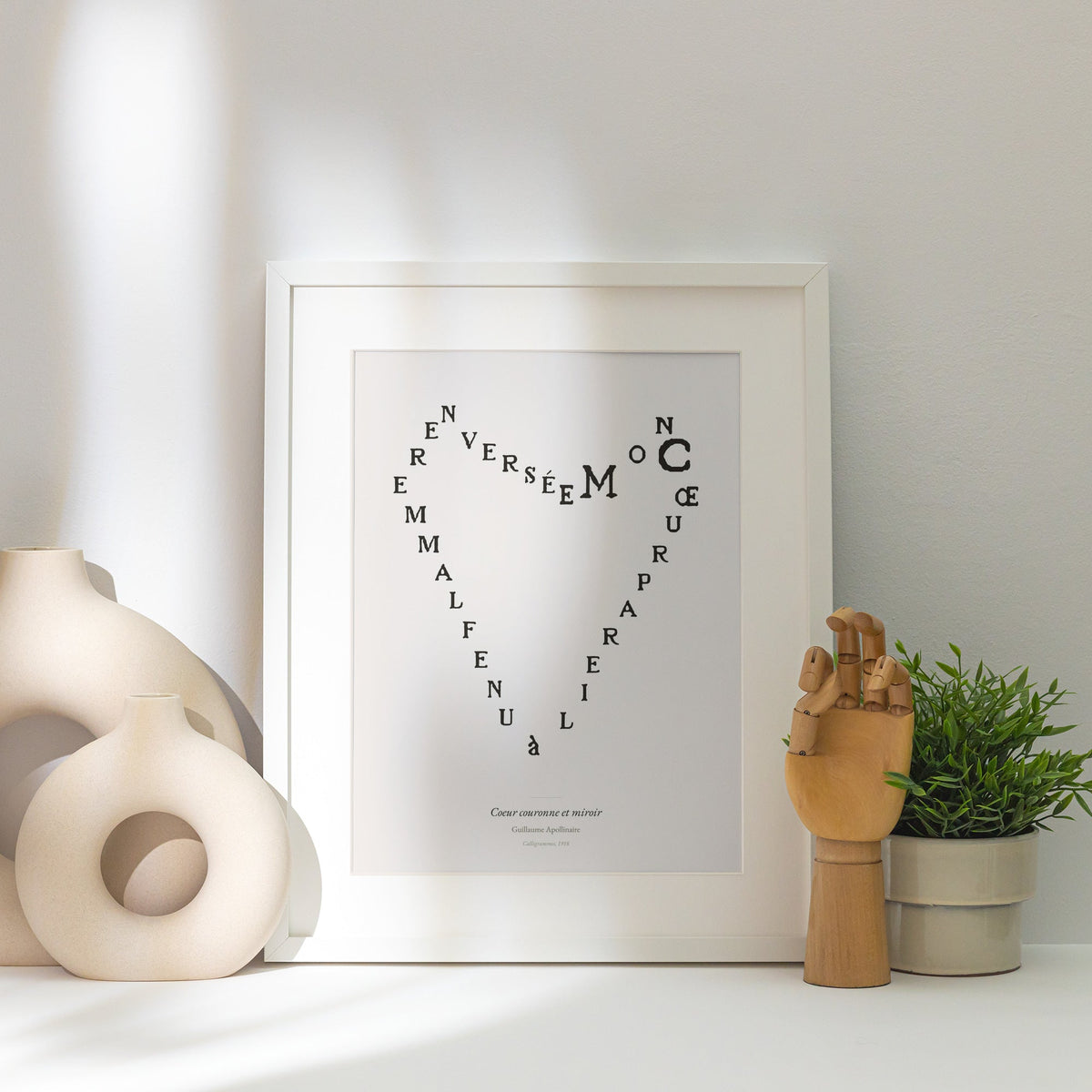 Coeur couronne et miroir, Guillaume Apollinaire, affiche encadrée posée près d'un vase blanc, lumière rasante
