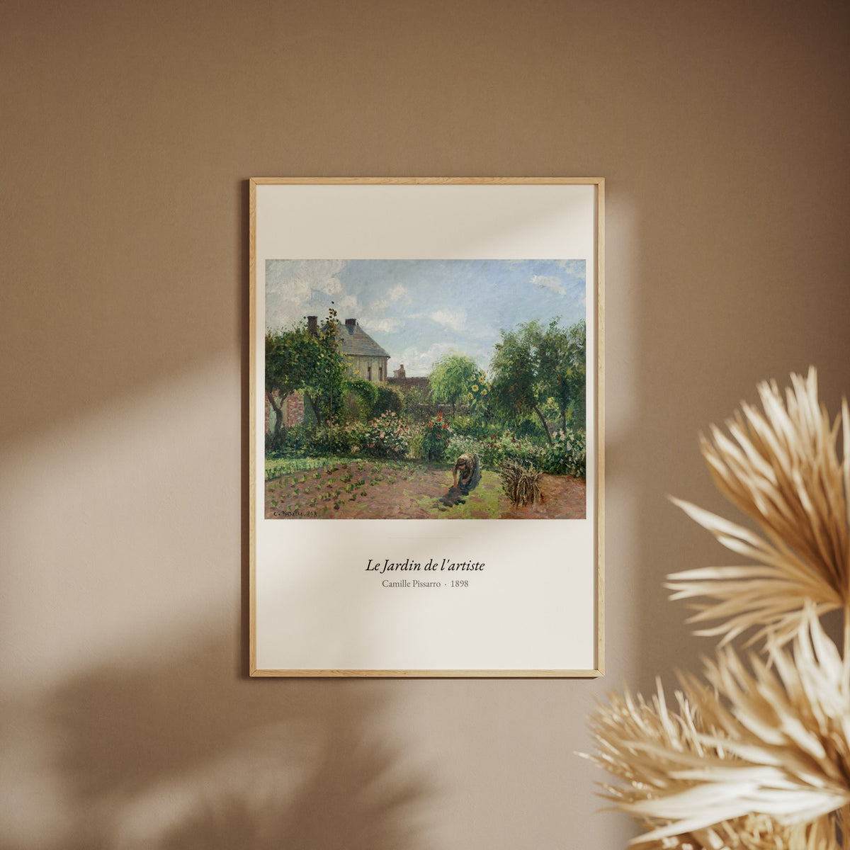 Le Jardin de l'artiste, Camille Pissarro, affiche encadrée sur un mur beige, pampas au premier plan