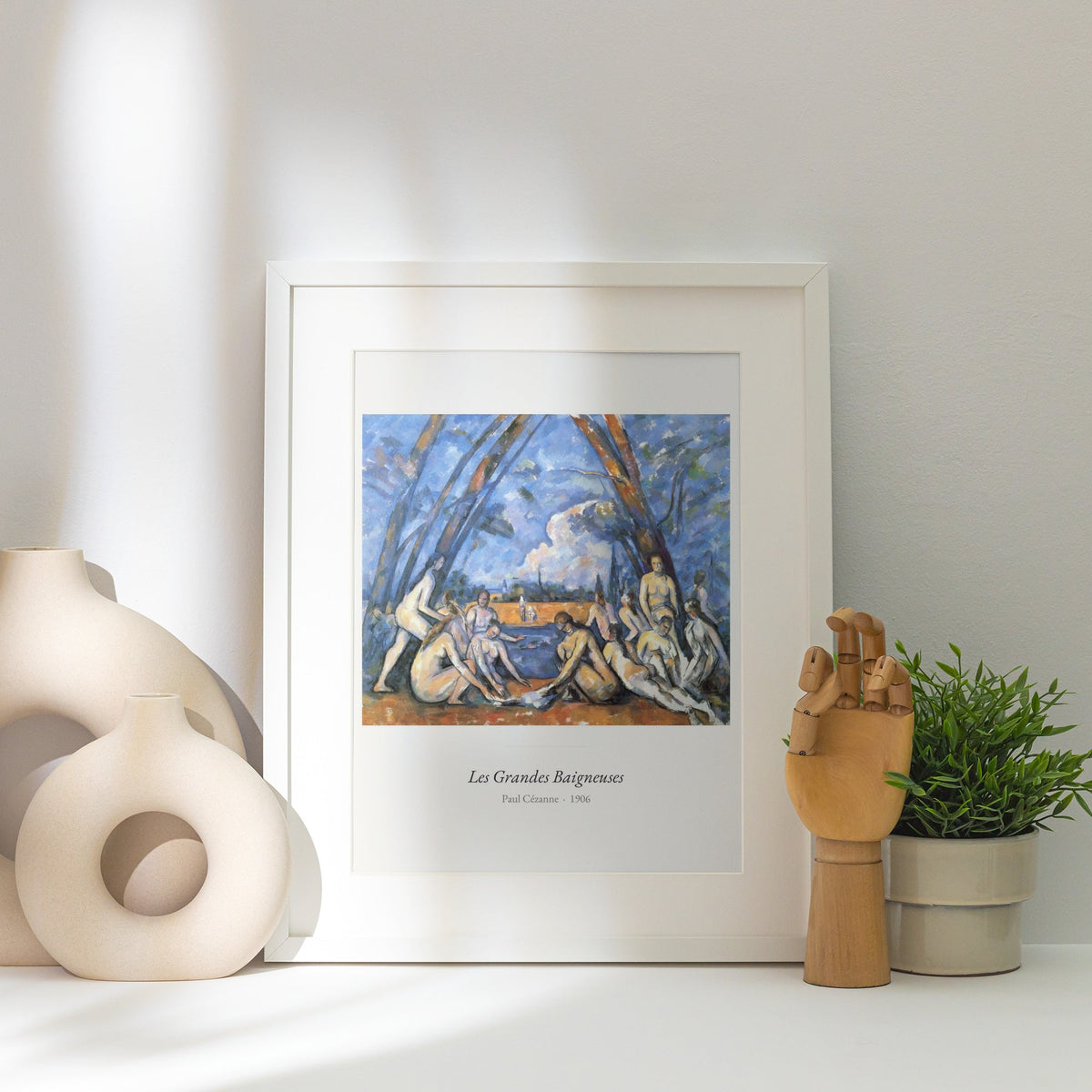 Les Grandes Baigneuses, Paul Cézanne, affiche encadrée posée près d'un vase blanc, lumière rasante