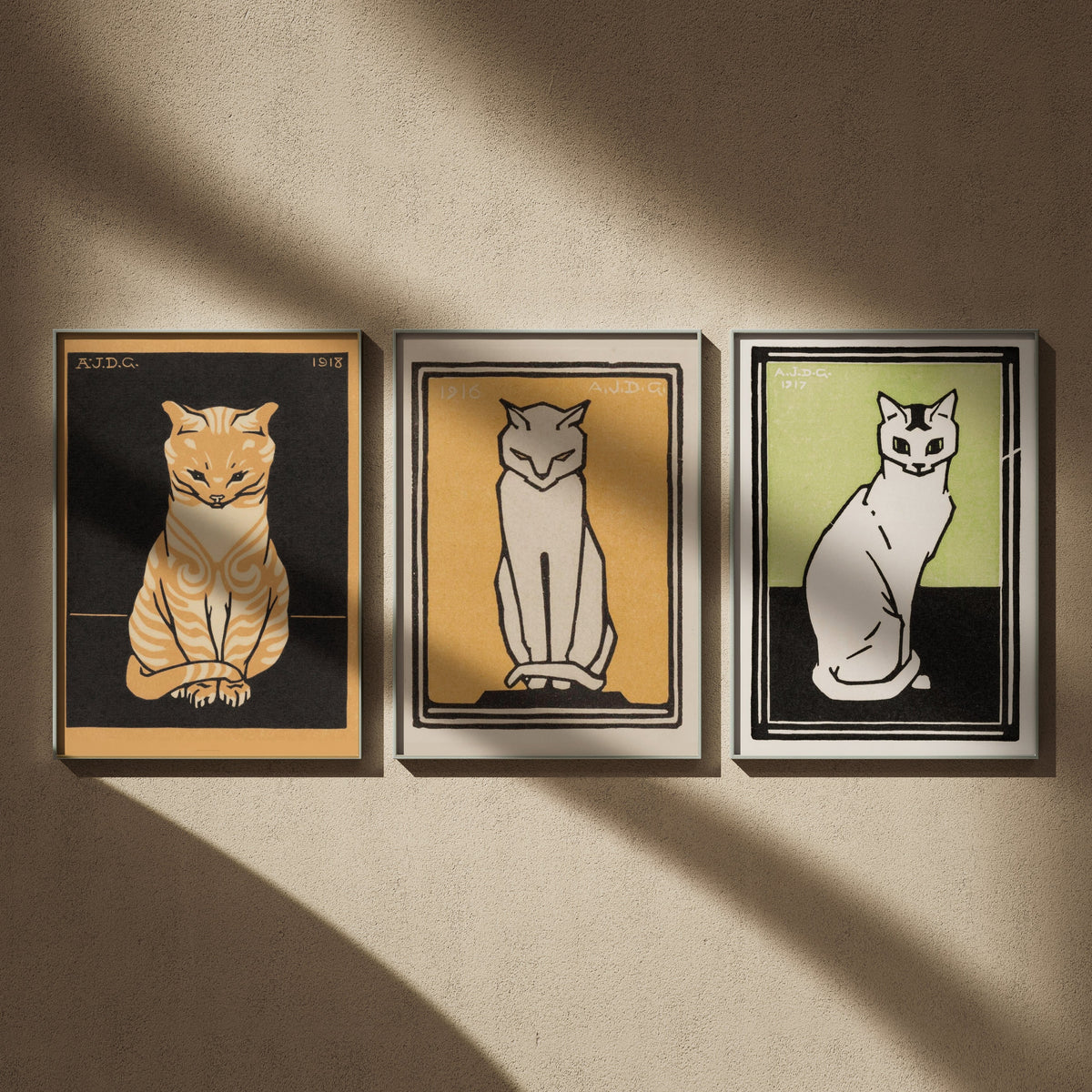 Triptyque chats de Julie de Graag en 50x70 : Chat assis, Chat blanc sur fond jaune et Chat blanc sur fond vert, encadrés côte à côte sur un mur beige