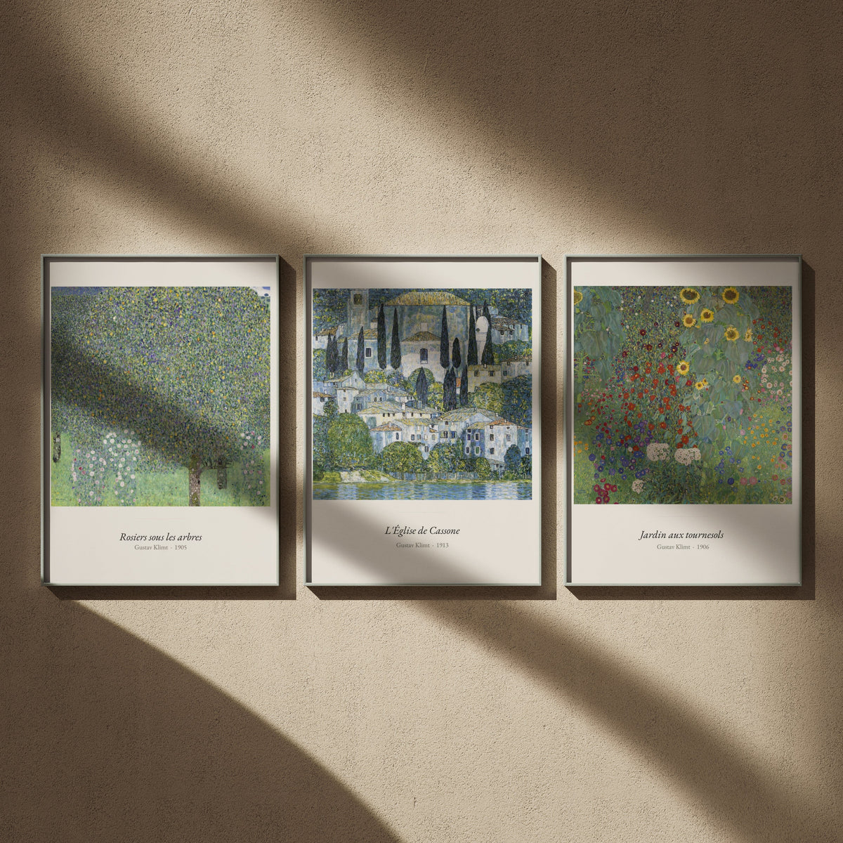 Triptyque Klimt paysages en 50x70 : Rosiers sous les arbres, L'Église de Cassone et Jardin aux tournesols, encadrés côte à côte sur un mur beige